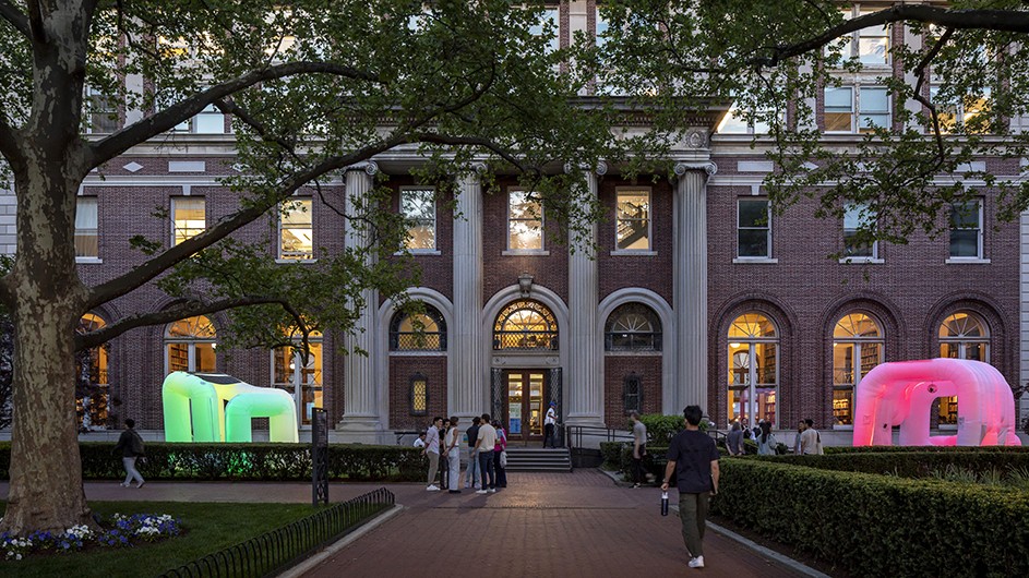 Several students in conversation near two illuminated inflatable canopies on either side of Avery Hall entrance at Columbia University at dusk.