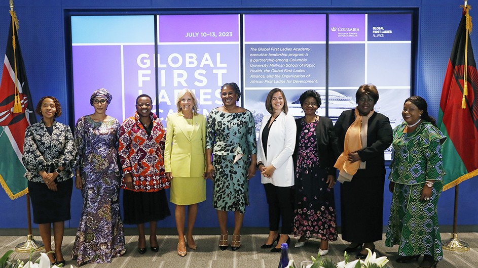 Seven First Ladies of Africa. First Lady Jill Biden, and alum Cora Neumann pose and smile on stage flanked by two African flags in front of Global First Ladies Alliance signage at Columbia University Irving Medical Center.