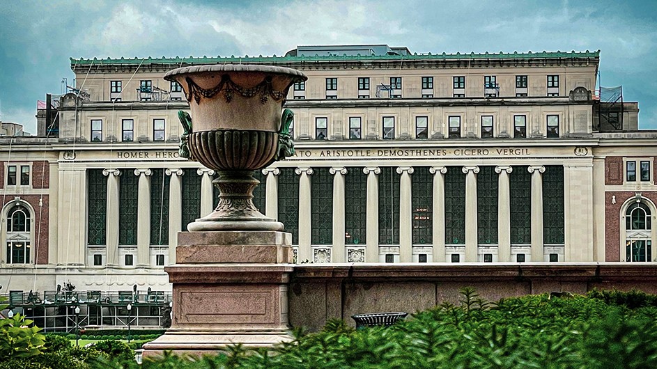 Construction-scaffolded Butler Library with a decorative stone urn in the foreground on a cloudy summer day at Columbia University.