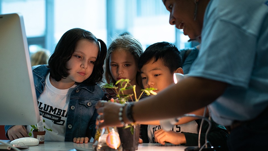 Three children observe a plant as an instructor gives them scientific information at Zuckerman Institute's Saturday Science at Columbia Manhattanville Community Day.