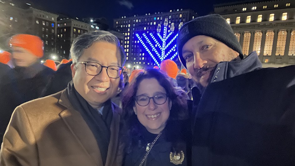 Engineering Dean Shih-Fu Chang, General Studies Dean Lisa Rosen-Metsch, and Columbia College Dean Josef Sorett smile and pose for the camera in front of a large Menorah on South Lawn at a Menorah Lighting event at Columbia University.  