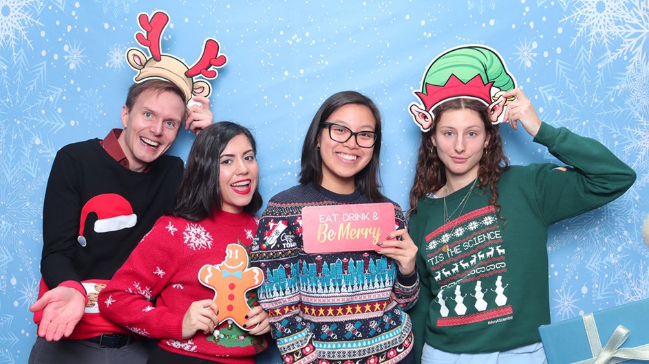 Four Columbia staff members wearing bright holiday sweaters and holding festive holiday hats and signs while posing for the annual "ugly" holiday sweater competition at Columbia medical center.