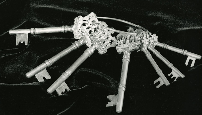 A black and white photograph of ornate keys on a velvet pillow