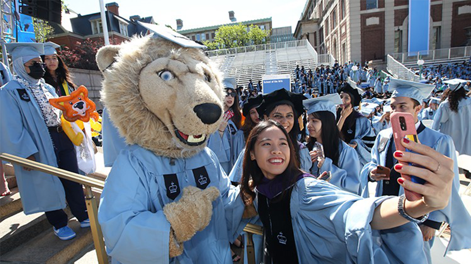 Columbia's mascot Roar-EE poses with a student during the academic procession. Photo by Bruce Gilbert.