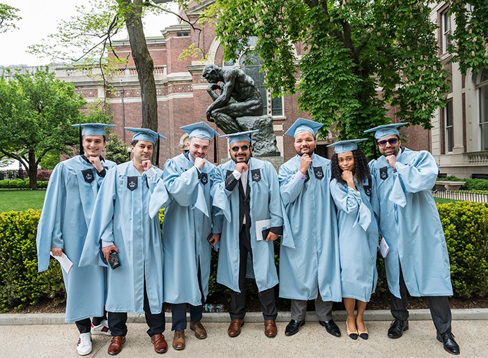 A group of graduates poses in front of the thinker statue. 