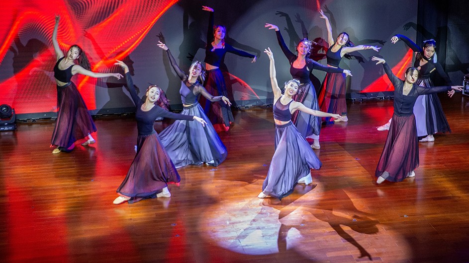 Nine students in dance attire glide across stage in a synchronized dance in celebration of Lunar New Year.