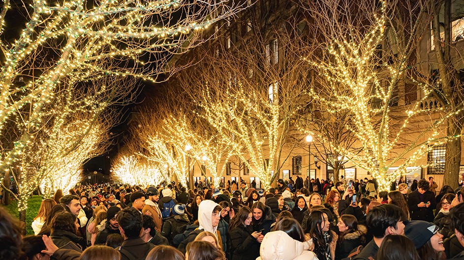 Dozens of college students gather to celebrate the holiday season as trees lining College Walk are illuminated with festive white lights in the evening at Columbia University.