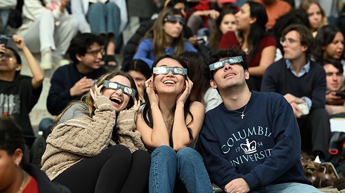 Three students look at the eclipse through eclipse glasses. 