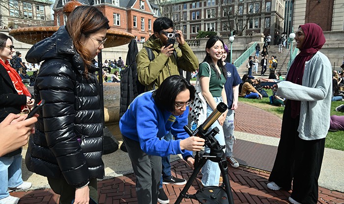 Astronomy department members help Columbians look at the eclipse through a telescope.