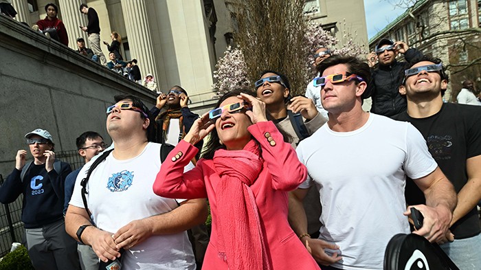 President Minouche Shafik looks up at the eclipse with eclipse glasses on.