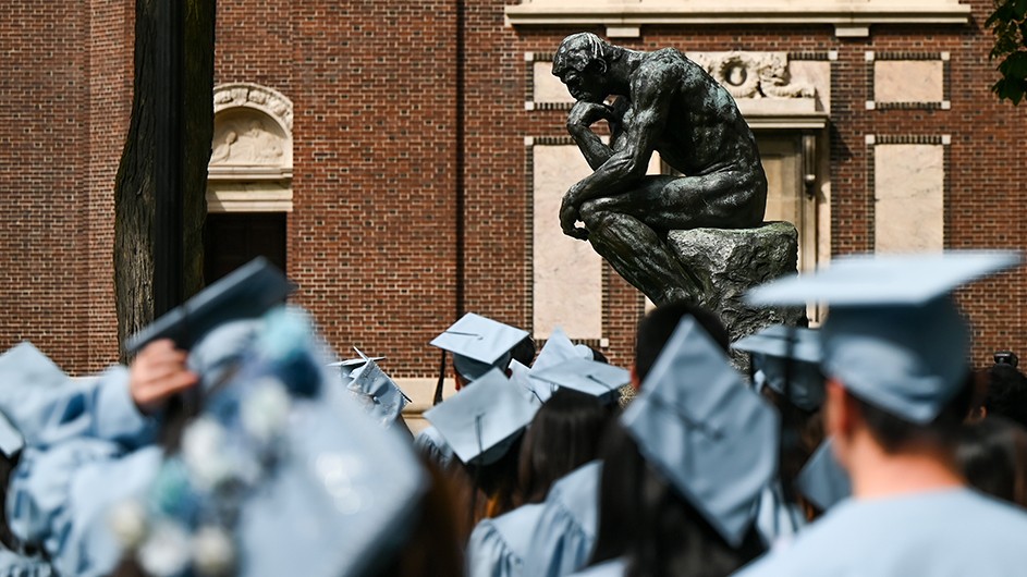 Columbia University graduates, in their robes, gather near The Thinker on the school's Morningside campus.