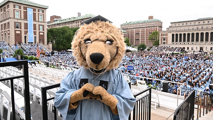 Nothing but love for the Class of 2025, straight from Roar-ee the Lion. Photo by Eileen Barroso. Roar-ee the Lion in Columbia regalia makes a heart with his hands in front of the Commencement crowd.