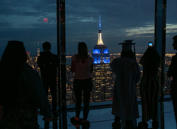 Columbia graduates take in the view of the Empire State Building from Summit One Vanderbilt. Photo by David Dini/Columbia University. The Empire State Building image ® is a registered trademark of ESRT Empire State Building, L.L.C. and is used with permission. The Empire State Building lit in blue as viewed from Summit One Vanderbilt.