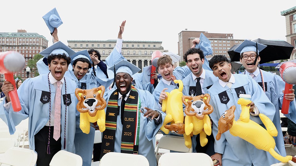 Eight university students wearing light blue graduation regalia cheer and roar while holding inflatable balloon lions and balloon hammers at Columbia Commencement on Morningside campus. 