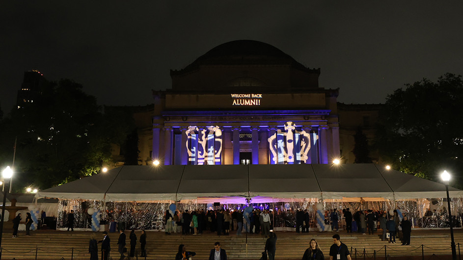 A tent filled with alumni underneath Low Library bearing lighting that reads "Welcome Back, Alumni!"