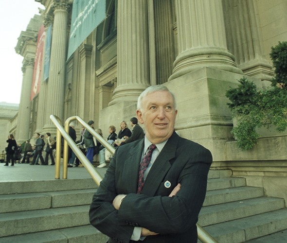 A man looking up cross-armed in front of a museum