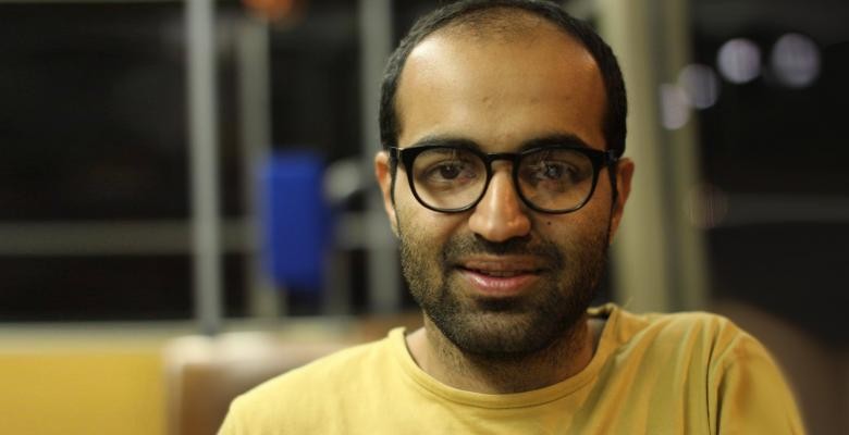 headshot of amir imani dressed in a yellow top with dark rimmed eyeglasses on