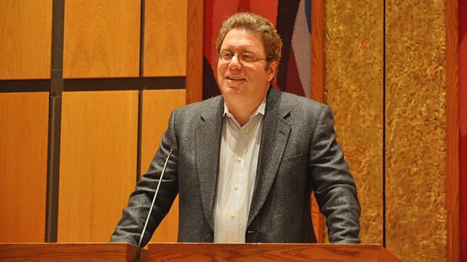 A man wearing a gray jacket and standing at a lectern.