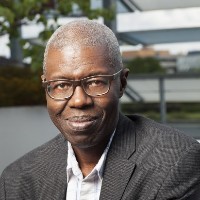 A headshot of a bespectacled African elderly man with grey hair 