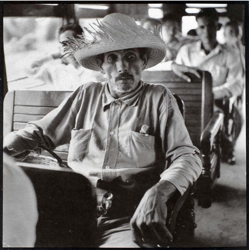 A man in a straw hat sitting on a wooden pew in a train. Photo Courtesy of the Delano Collection at Rare Book and Manuscript Library