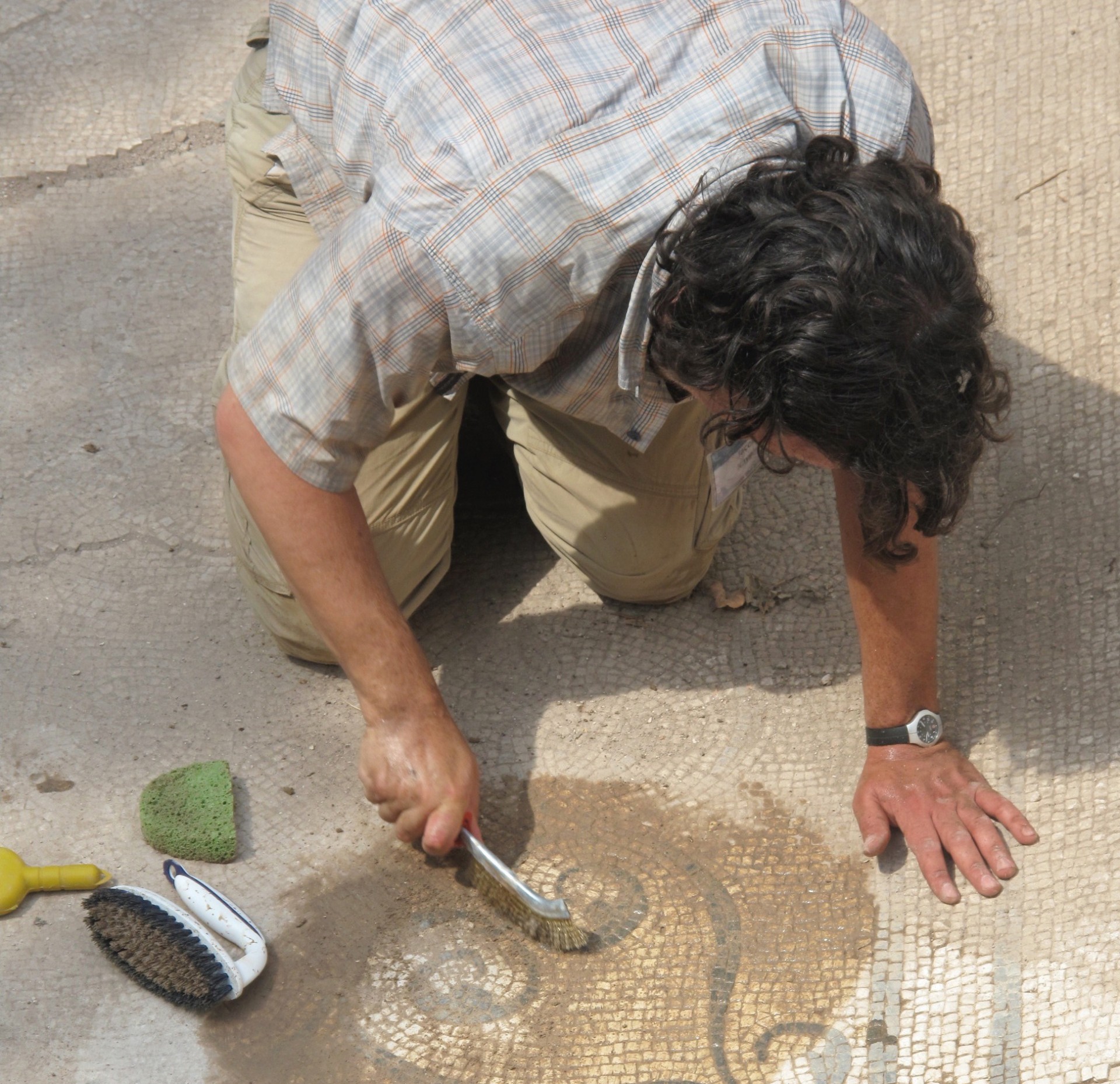 Advanced Program of Ancient and Art History participant removing limestone concretions from the surface of a mosaic floor. Photo by F. de Angelis A man washes away dirt from a floor mosaic