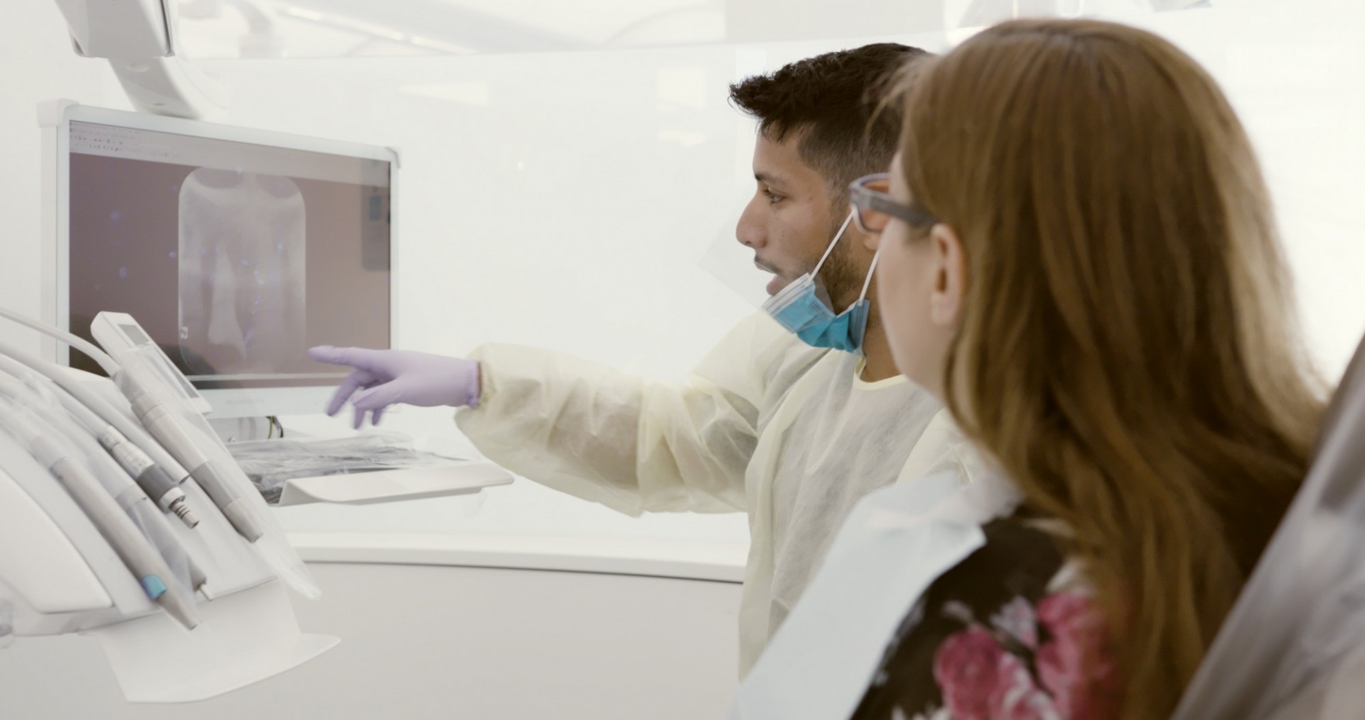 A dentist points a patient to a computer screen