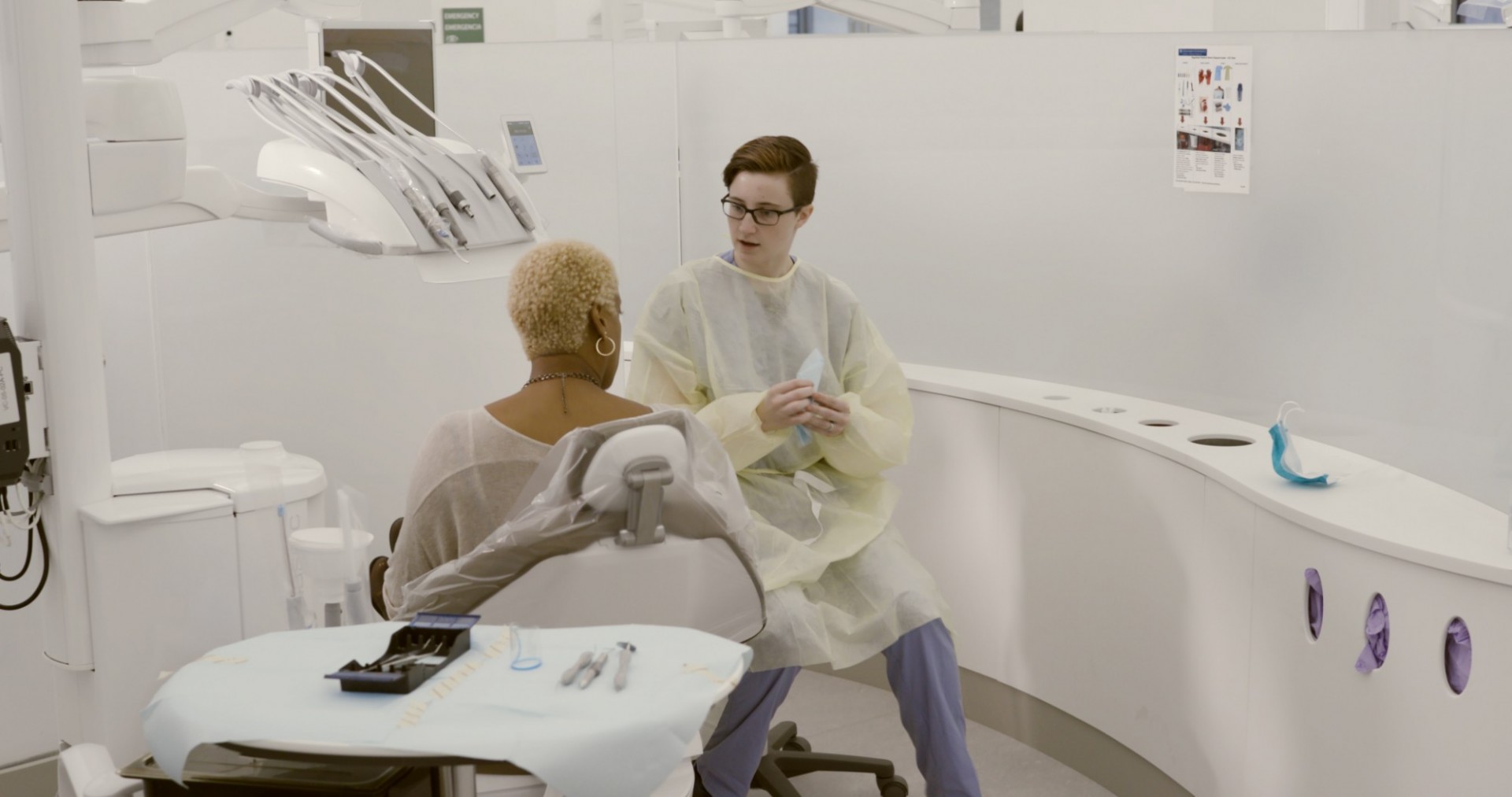 A dentist speaks to a patient in a dental chair