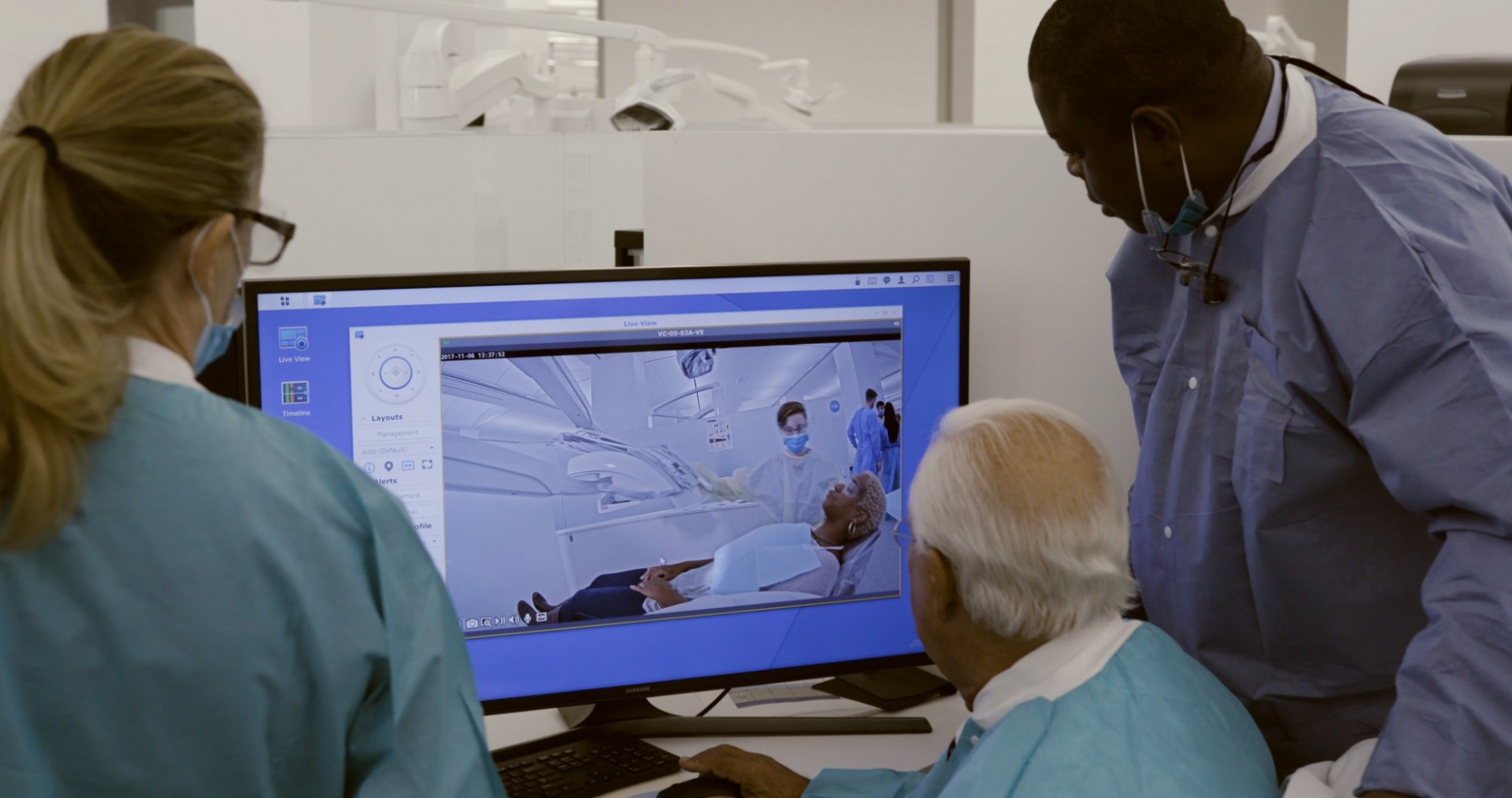 Two dentists look at a computer screen over a third dentist's shoulder