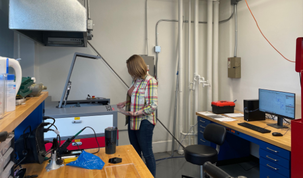 Clara Wilson standing in front of laser cutter, with a computer behind her.