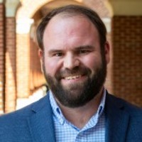 Robert Colby: A man with brown hair and beard, smiling, wearing a blue suit jacket and blue button-down shirt.