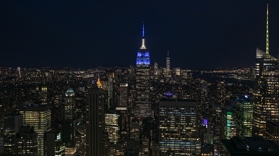 New York City skyline at night with the Empire State Building lit blue.