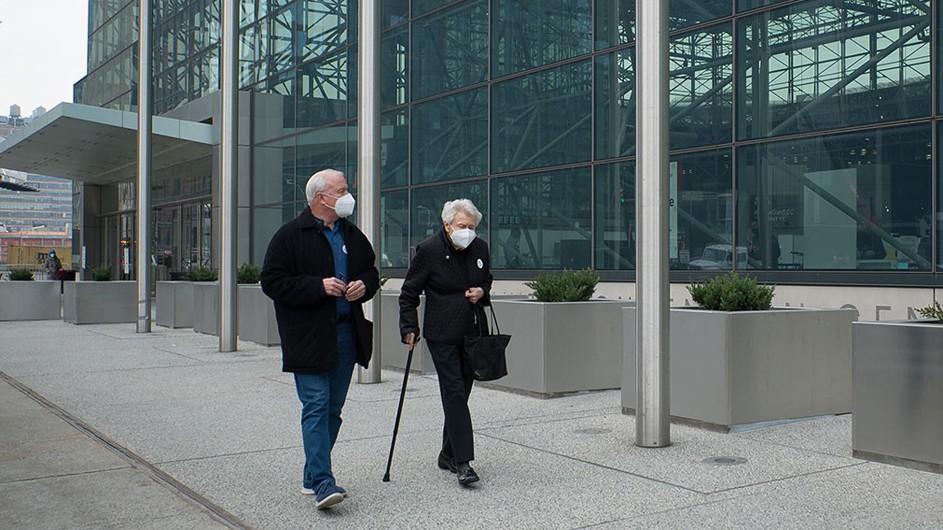 elderly man and woman wearing white masks walking on city sidewalk