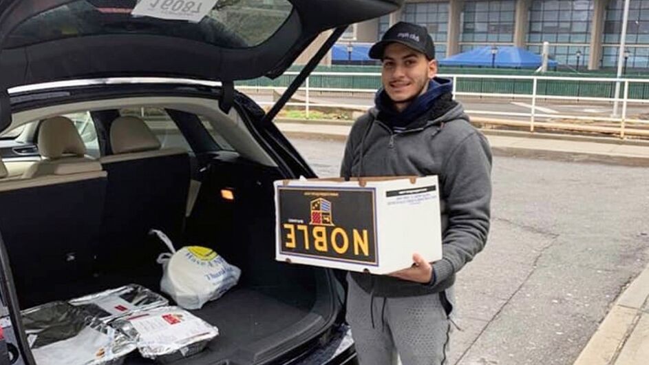 Eytan Israelov drops off food from his family's restaurant for health workers at Long Island Jewish Medical Center. young man with blue cap and grey jacket takes boxes out of runk of car in front of hospital