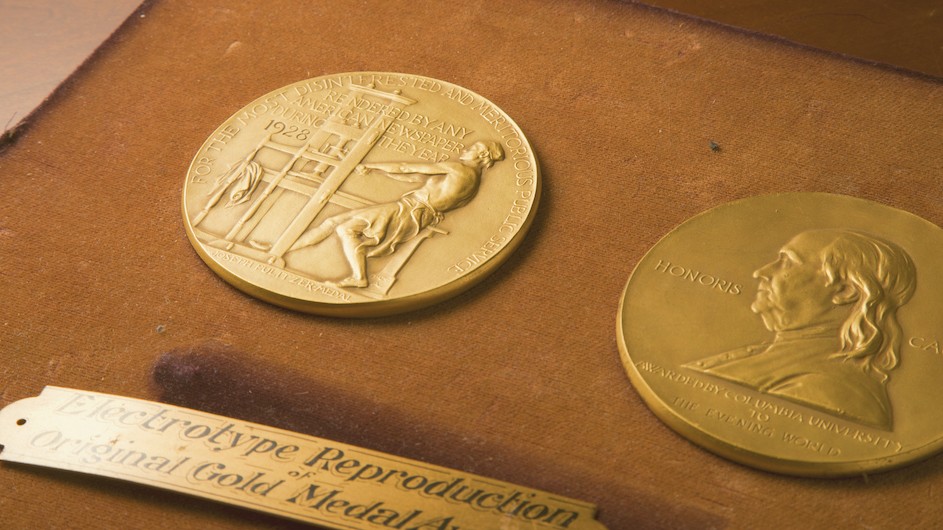 Two gold coin Pulitzer medals on a brown board