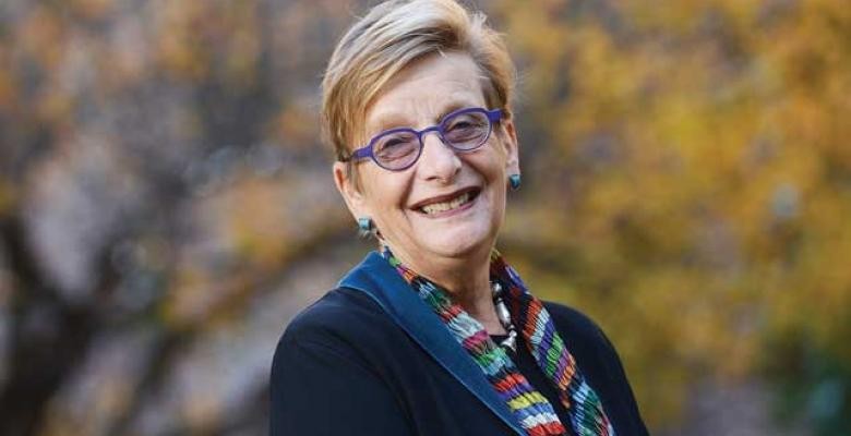 Marianne Hirsch smiles into camera wearing purple rimmed eyeglasses dark colored coat with a colorful scarf draped around neck