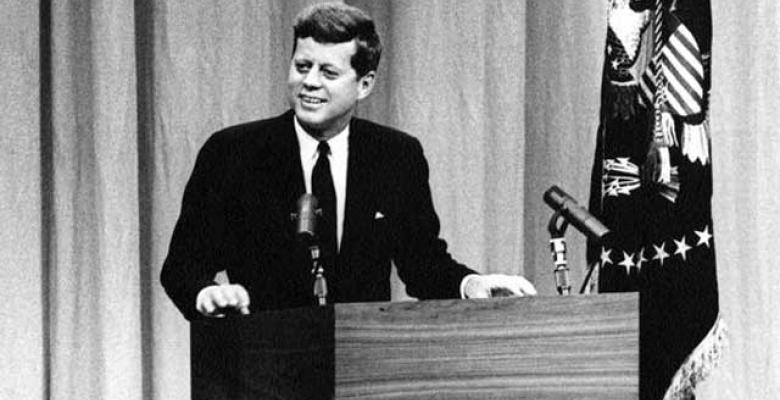 President John F. Kennedy smiles from stage at press conference, State Department Auditorium, Washington, D.C. Credit Line: Abbie Rowe. White House Photographs. John F. Kennedy Presidential Library and Museum, Boston