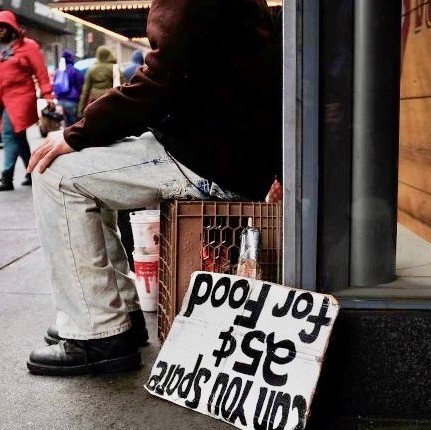 Man sitting on a box in NYC with a sign asking for food