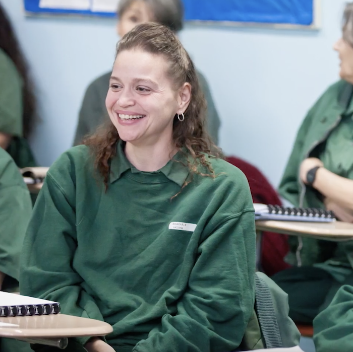 Woman in green shirt smiling at a classroom desk