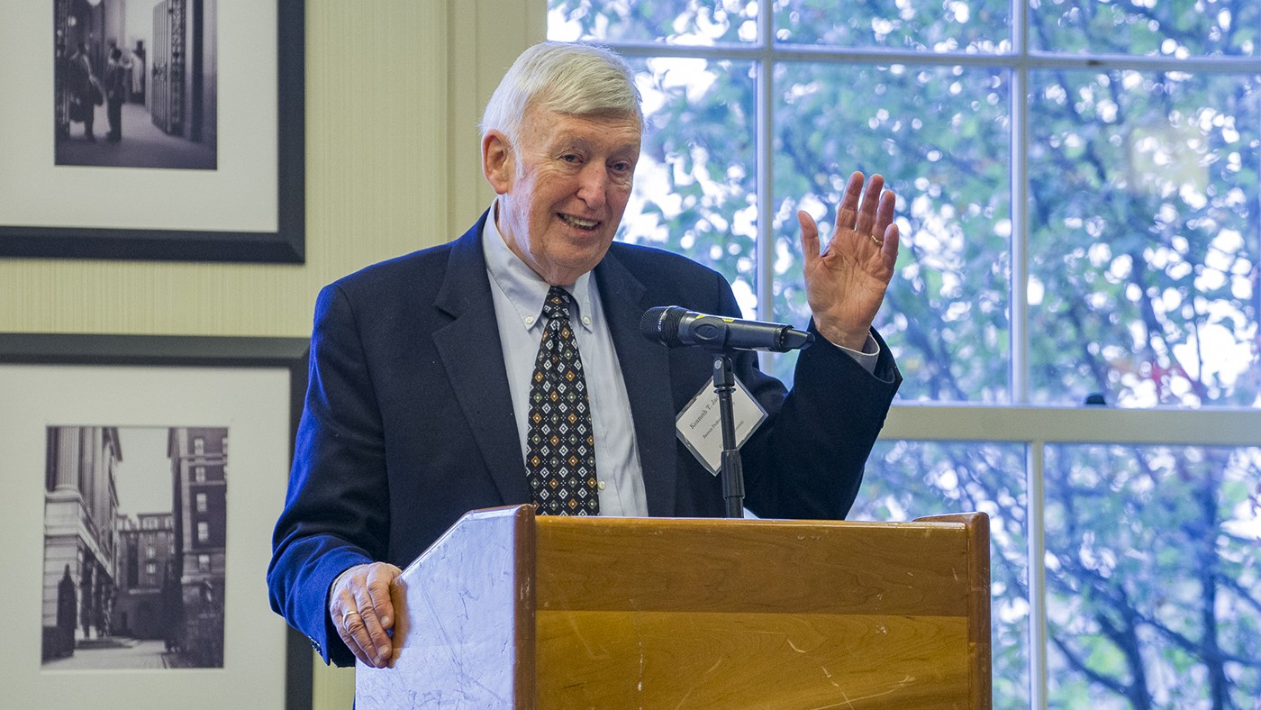 A speaking behind a podium with his hand up