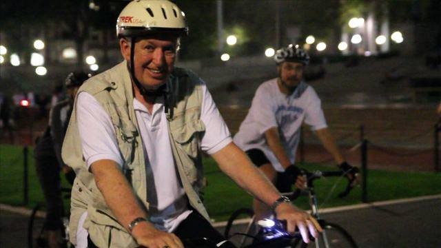 Two men wearing helmets riding bicycles at night