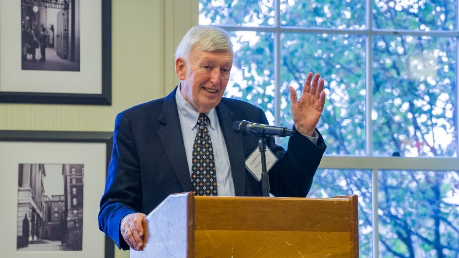A man speaking behind a podium with his hand up