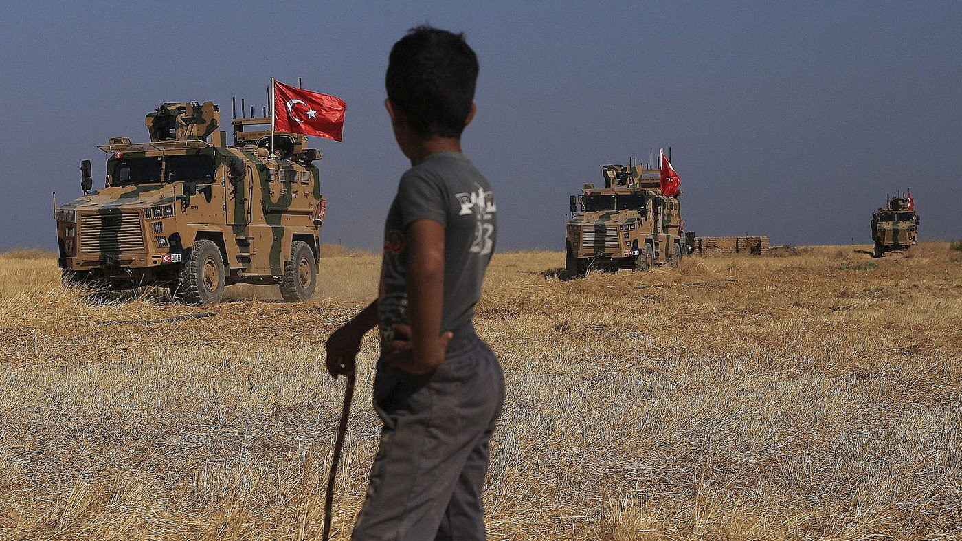 Turkish armored vehicles patrol the "safe zone" of the Syrian border with Turkey, near the town of Tal Abyad, northeastern Syria, October 4, 2019. (AP Photo/Baderkhan Ahmad) A boy watching the armed trucks with Turkish flags driving by.