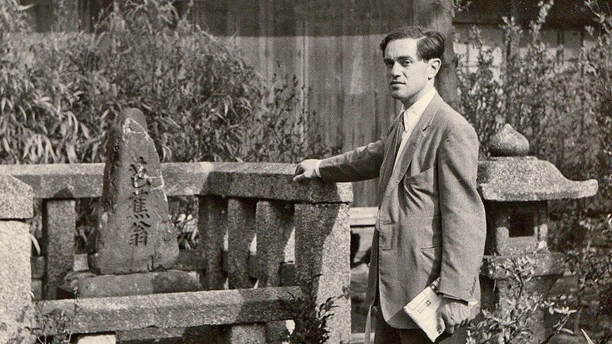 Donald Keene at poet Basho’s tomb in Zeze, Japan, 1955. (Courtesy of Seiki Keene) An old black and white photo of a man standing wearing a suit.