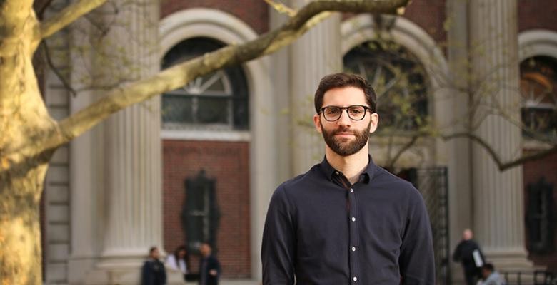 headshot of Majad Abdulsamad dressed in dark shirt with dark rimmed eyeglasses standing on campus of Columbia University