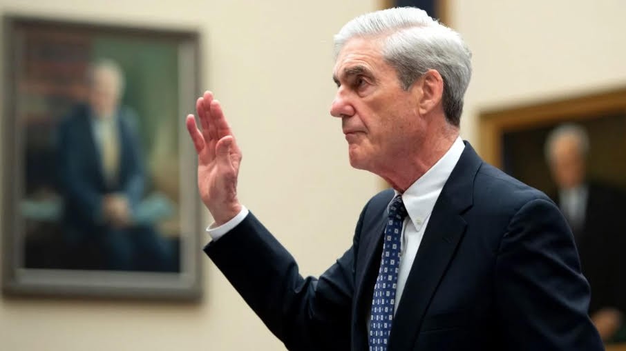 Robert Mueller testifying before Congress. A gray haired man in suit with his hand raised to take an oath