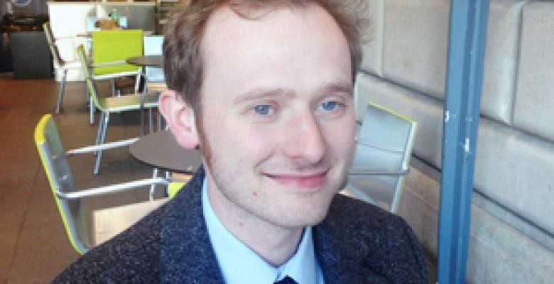 A young man with red hair and blue eyes smiles at the camera