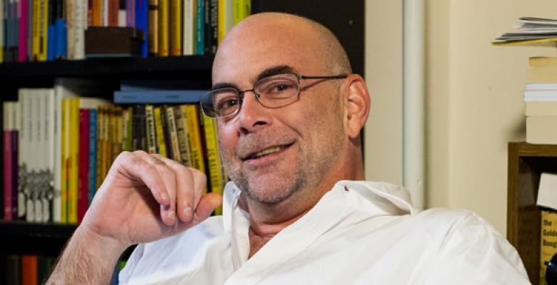 A smiling middle-aged man with glasses leans back in his chair