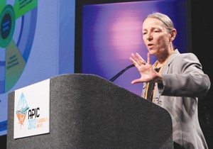 A woman stands at a podium, gesturing with her hands as she speaks 