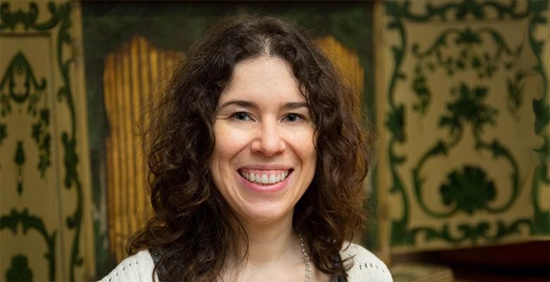 A woman with shoulder-length curly brown hair smiles into the camera