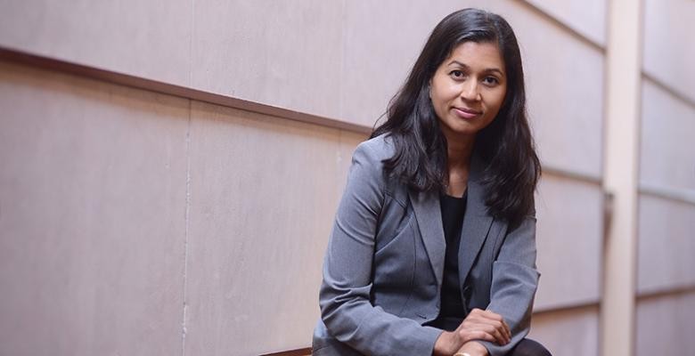 Photo by Eileen Barroso A woman with shoulder-length hair and wearing a gray suit looks directly into the camera, standing against the facade of a building